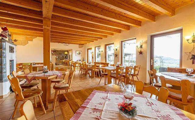 Innenansicht eines Restaurants mit Holzdecke und Tischen. Es gibt Stühle, eine dekorierte Tischdecke und eine Wand mit einem Kamin.