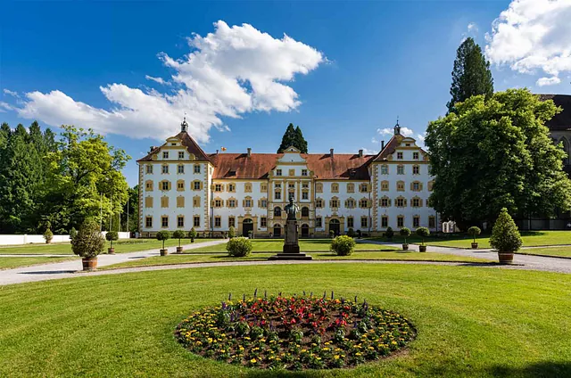 Schloss Salem, ein großes, historisches Gebäude mit gelber Fassade und roten Dächern, umgeben von einem gepflegten Garten mit Blumenbeeten und Bäumen.