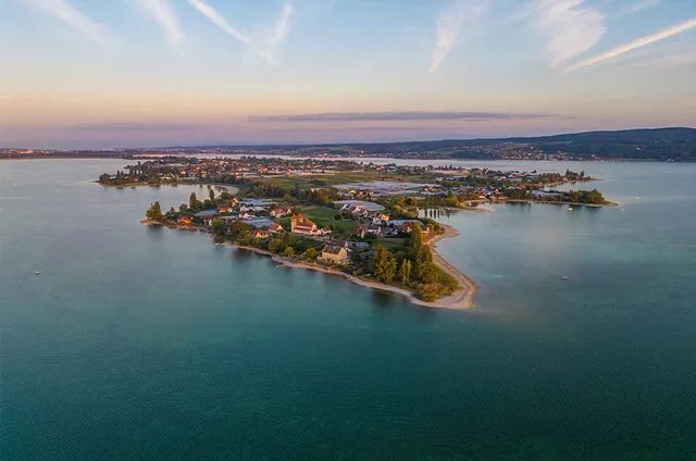 Luftaufnahme der Insel Reichenau im Bodensee, umgeben von Wasser und mit mehreren Gebäuden und Bäumen auf der Insel. Sichtbare Beschriftung: 'Insel REICHENAU'.