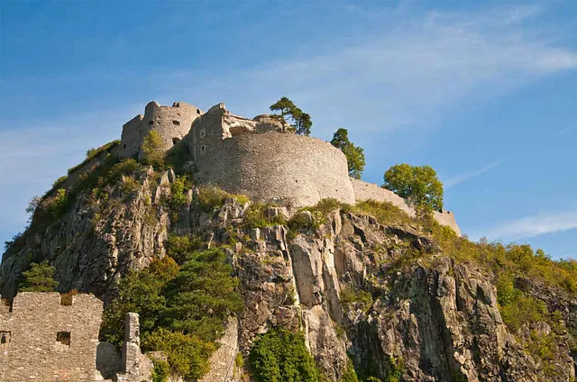 Blick auf die Festungsruine Hohentwiel in Singen, auf einem bewaldeten Hügel, mit steilen Felsen im Vordergrund. Sichtbare Mauerreste und Bäume.