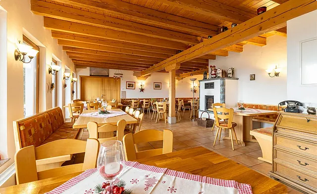 Innenansicht eines Restaurants mit Holzbalkendecke, Tischen und Stühlen aus Holz. Tischdecken mit rot-weißen Mustern, Fenster mit Blick ins Freie.